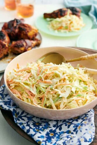 A bowl of coleslaw with spoons tucked in. Grilled chicken in the background.
