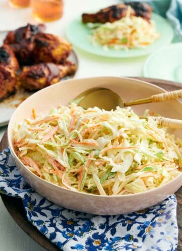 A bowl of coleslaw with spoons tucked in. Grilled chicken in the background.