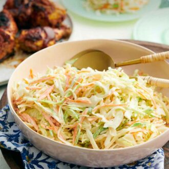 Pinterest graphic of a bowl of coleslaw with spoons tucked in. Grilled chicken in the background.