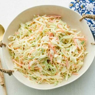 A serving plate of coleslaw with serving spoons on the side along with a napkin.