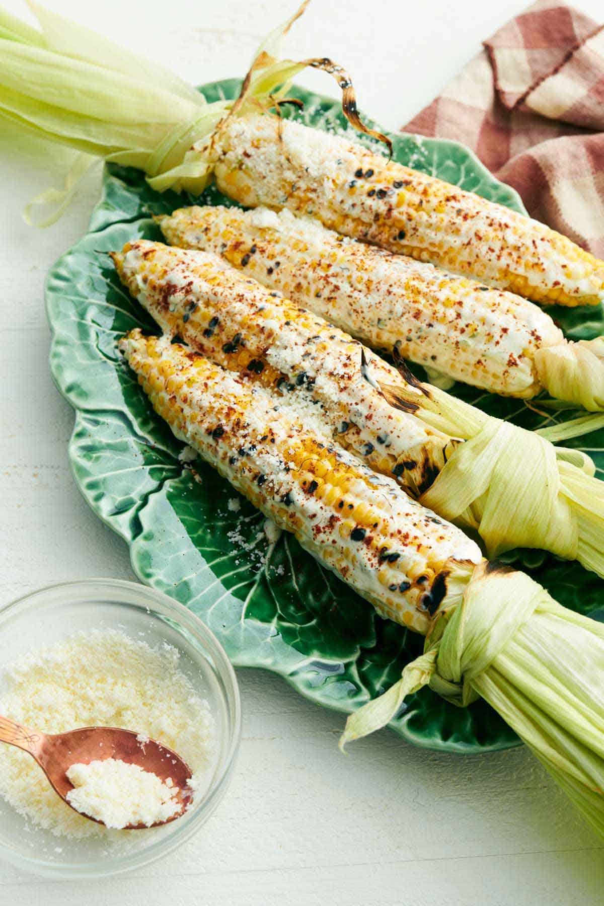 A lettuce-shape platter of elote with a bowl of cotija cheese in front.