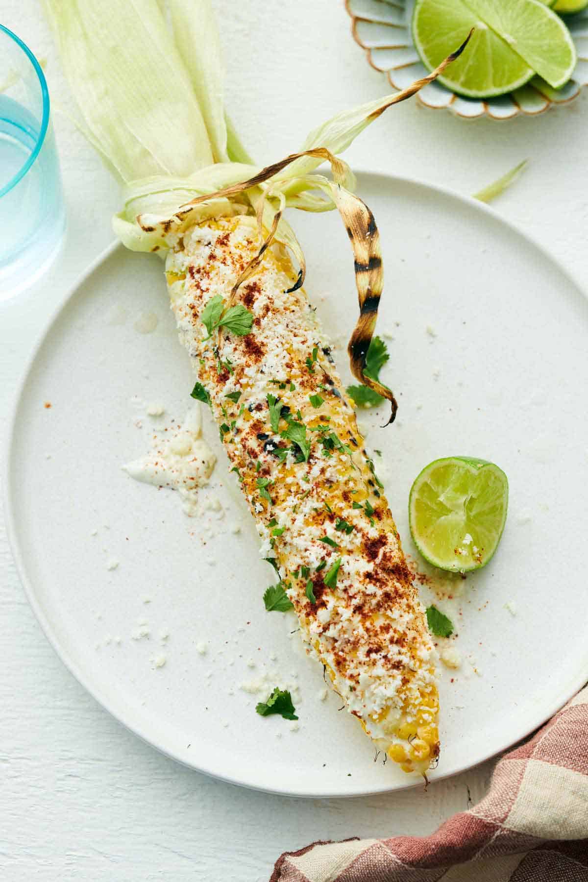 Overhead view of a plate with an elote topped with cilantro with a lime wedge beside it.