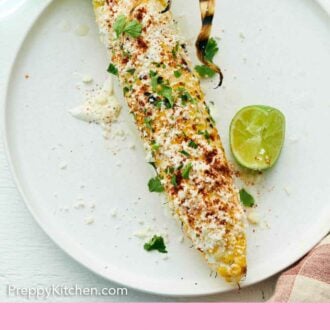 Pinterest graphic of a plate with an elote topped with cilantro with a lime wedge beside it.