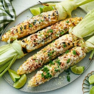 Overhead view of a platter with four elote topped with cilantro with limes on the side.