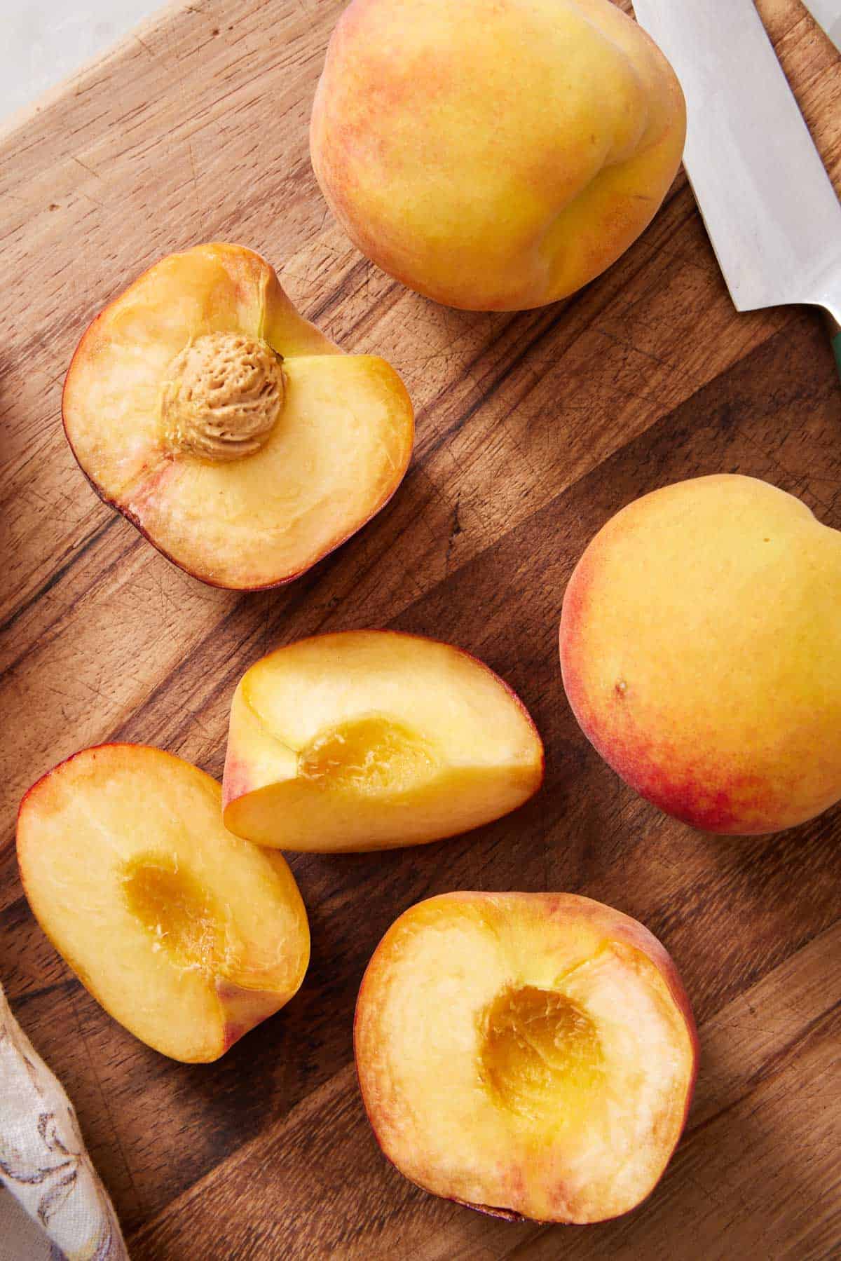 Peaches being cut in half and quarters on a cutting board.