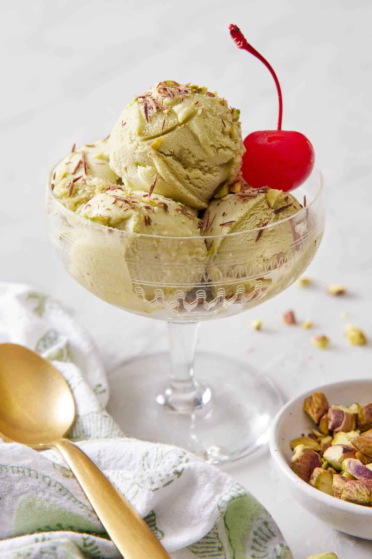 An ice cream serving bowl with multiple scoops of pistachio ice cream with a cherry.