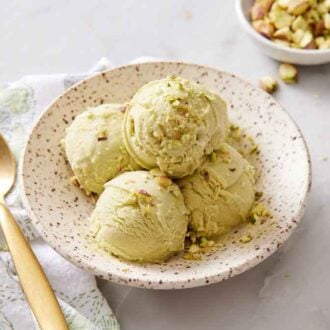 A bowl with multiple scoops of pistachio ice cream. A spoon beside it.