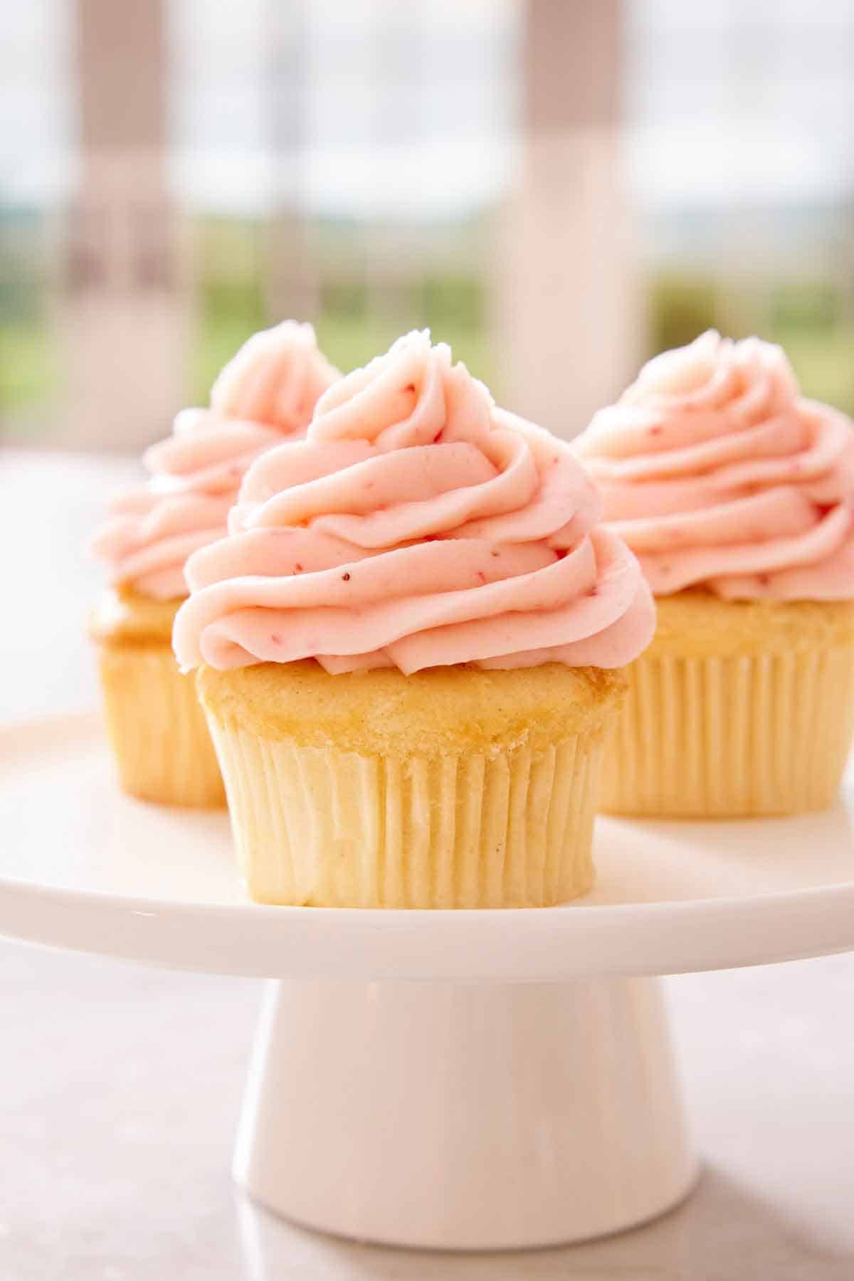 A cake stand with three cupcakes with strawberry frosting.