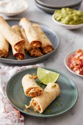 An air fryer taquito cut in half on a green plate with a lime wedge. More taquitos in the background.