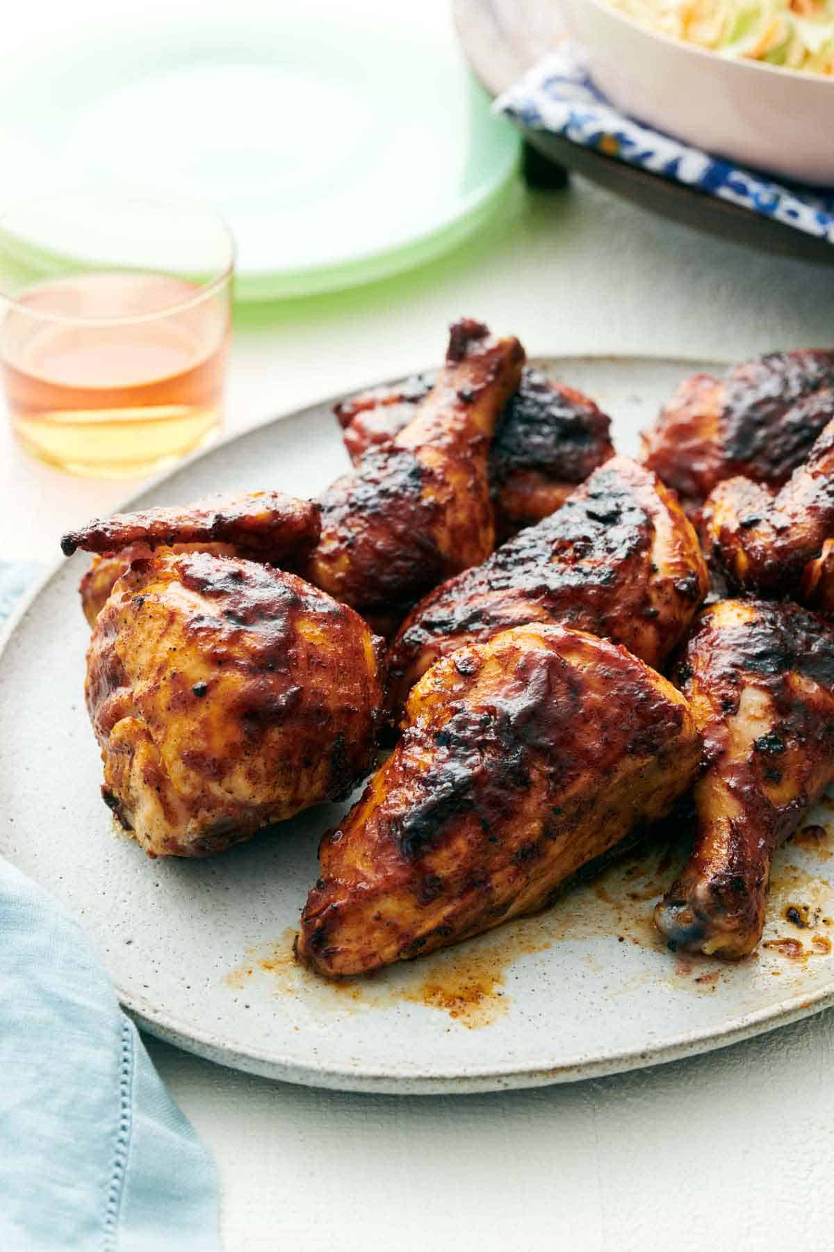 A platter of BBQ chicken with a drink in the background.