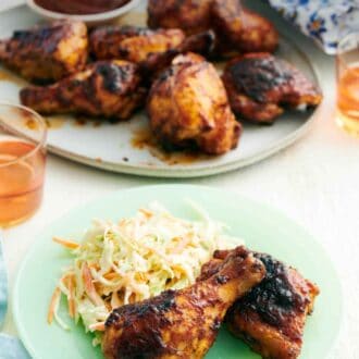 Pinterest graphic of a plate with two pieces of BBQ chicken and coleslaw with a platter of more BBQ chicken in the background.