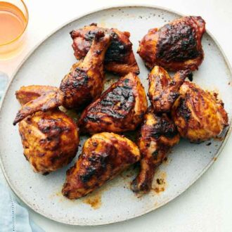 Overhead view of a platter of BBQ chicken with a drink beside it.