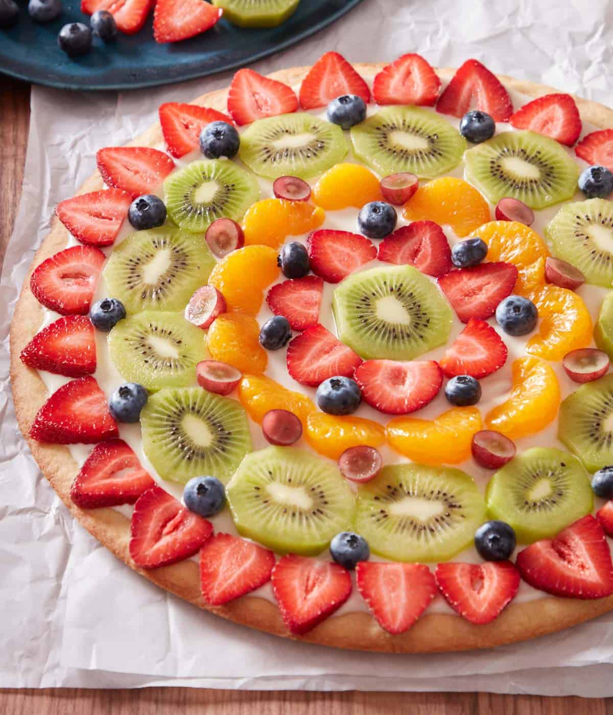 A fruit pizza on a parchment-lined serving board.
