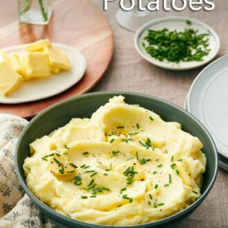 Pinterest graphic of a bowl of garlic mashed potatoes with chives, pepper, and butter on top. More butter in the background, chives, and glasses of water.