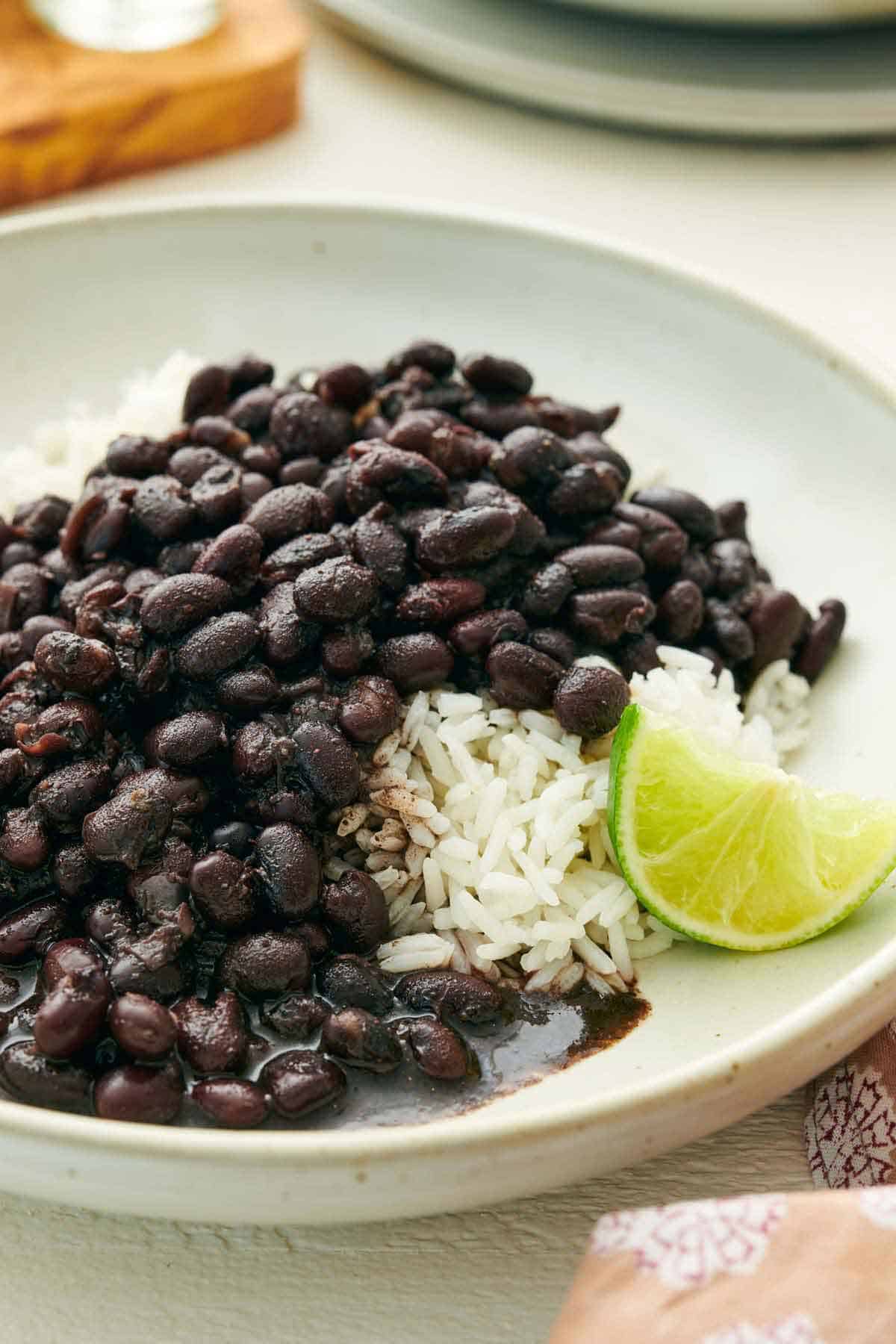 A close up view of a plate of Instant Pot black beans over rice with a wedge of lime.