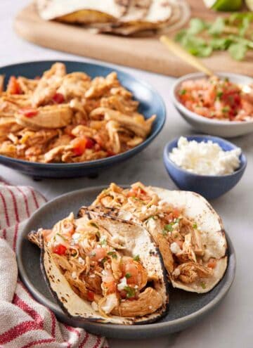 A plate with two Instant Pot chicken tacos with the rest of the components in the background.