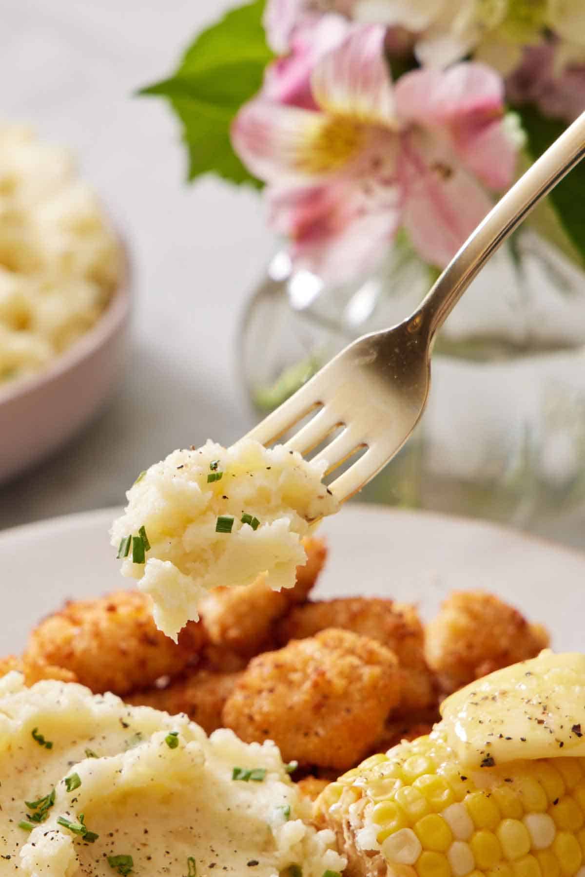 A fork lifting up a bite of Instant Pot mashed potatoes from a plate.