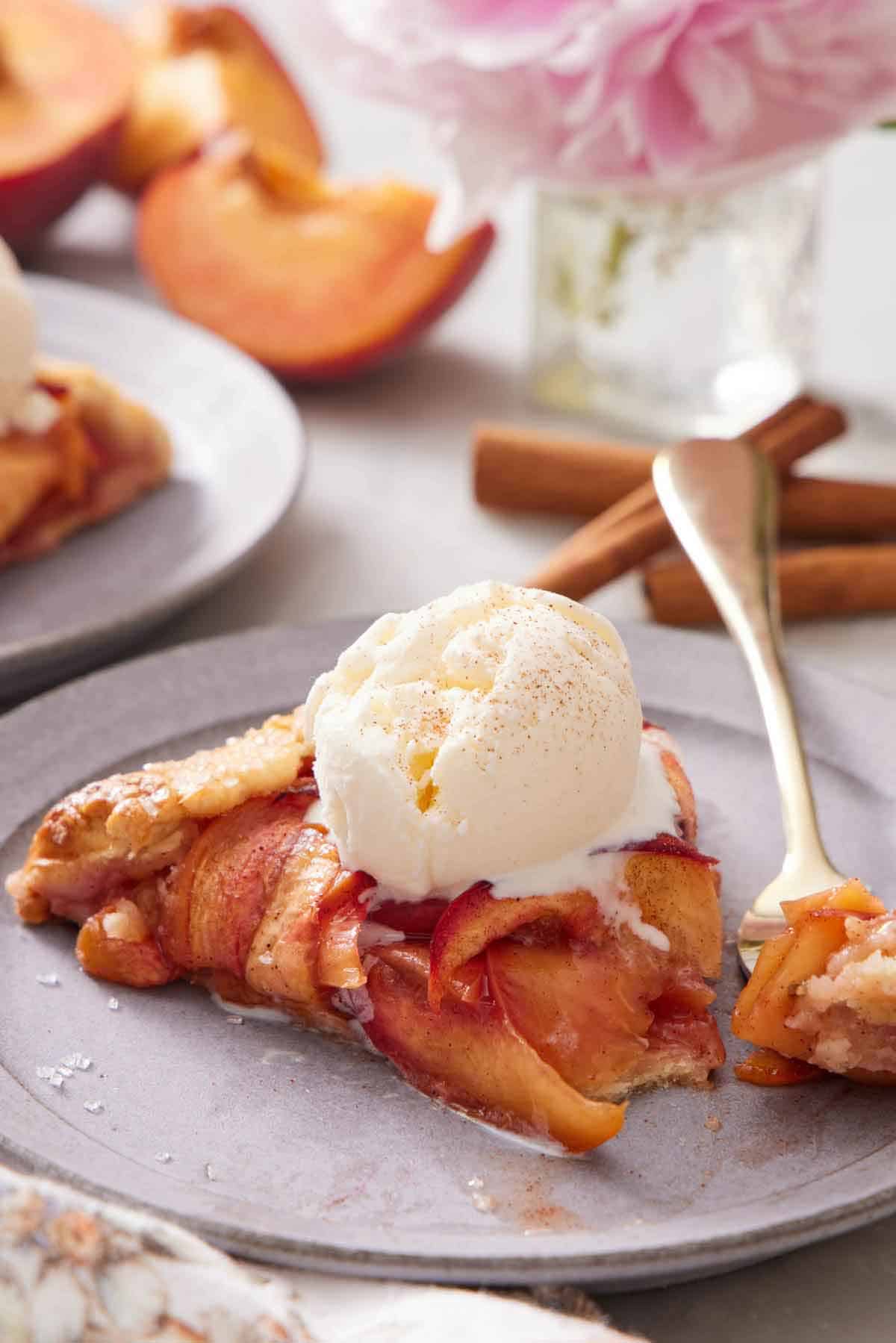 A slice of peach galette with a scoop of ice cream with a fork with a bite scooped onto it.