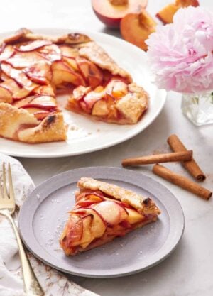 A plate of peach galette on a plate with the rest of the galette in the background.