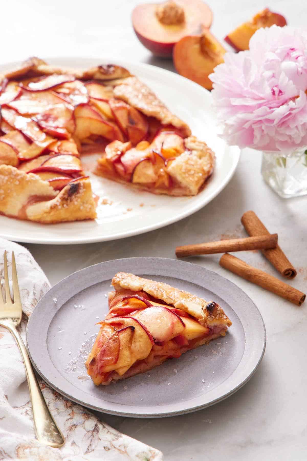 A plate of peach galette on a plate with the rest of the galette in the background.