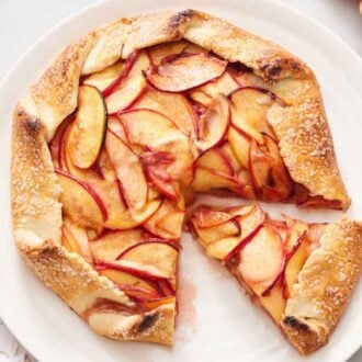 A platter with a peach galette with a slice cut out and another slice sliced and pulled out.