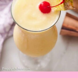 Pinterest graphic of a slightly overhead view of a glass of piña colada with a straw, pineapple slice, and a maraschino cherry.