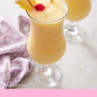 Pinterest graphic of a glass of piña coladas with a straw, pineapple slice, and a maraschino cherry. A purple napkin beside it.