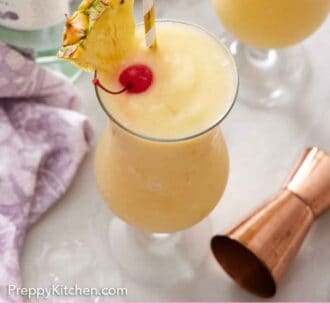 Pinterest graphic of a slightly overhead view of two glasses of piña colada, each with a straw, pineapple slice, and a maraschino cherry. A jigger and bottle of rum beside them.