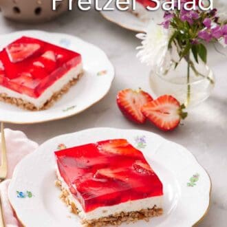 Pinterest graphic of plates of sliced strawberry pretzel salad with a vase of flowers and bowl of strawberries between them.