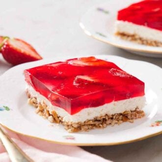 A square slice of strawberry pretzel salad on a plate with a second serving in the background.