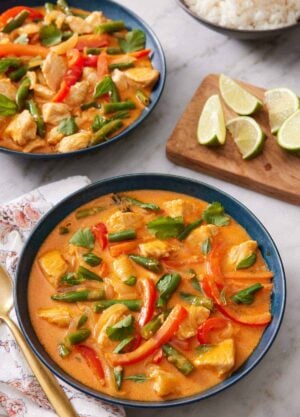 Two bowls of Thai red curry with a wooden board with lime wedges in between.