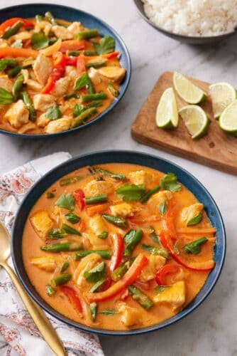 Two bowls of Thai red curry with a wooden board with lime wedges in between.