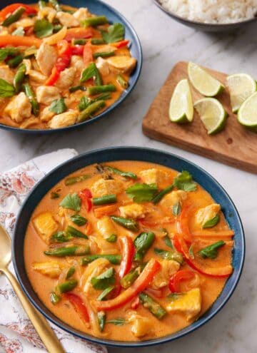 Two bowls of Thai red curry with a wooden board with lime wedges in between.