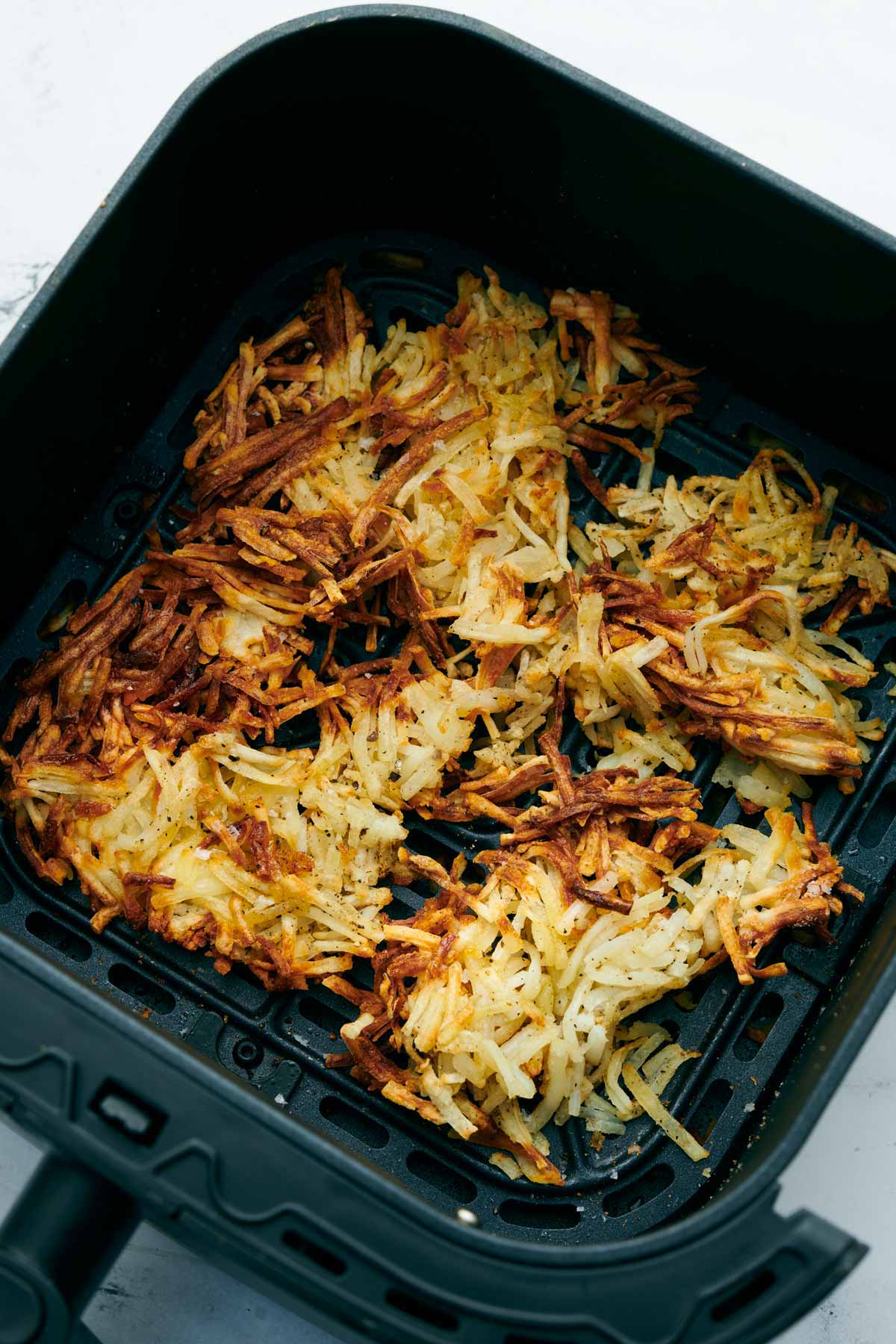 Overhead view of crispy hash browns in an air fryer basket.