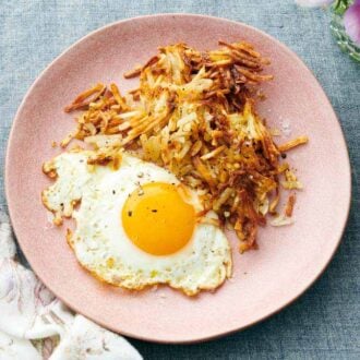 A plate with air fryer hash browns and a fried egg. A napkin beside the plate.