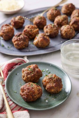 A plate with three air fryer meatballs with a platter more in the background with a drink in-between.