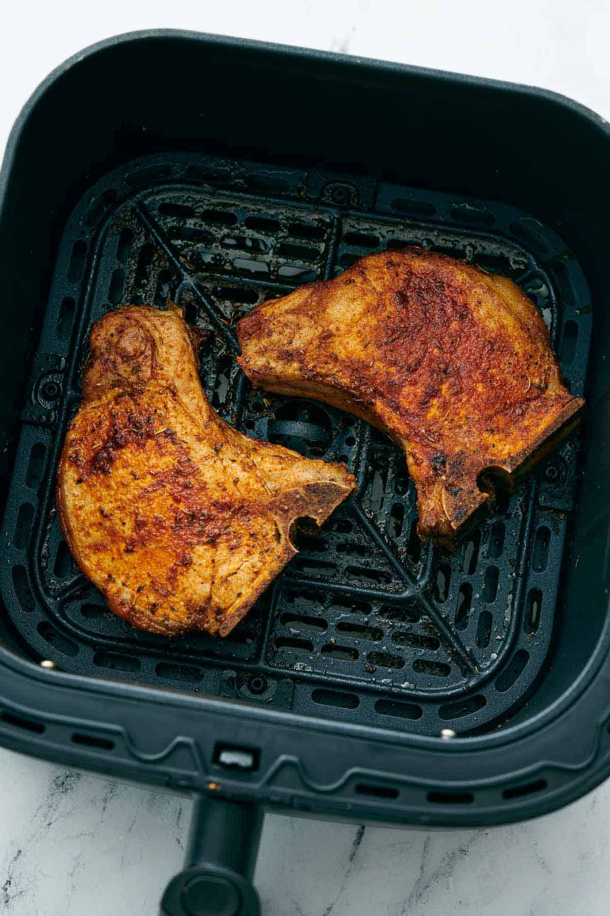 Overhead view of two pork chops in an air fryer basket.