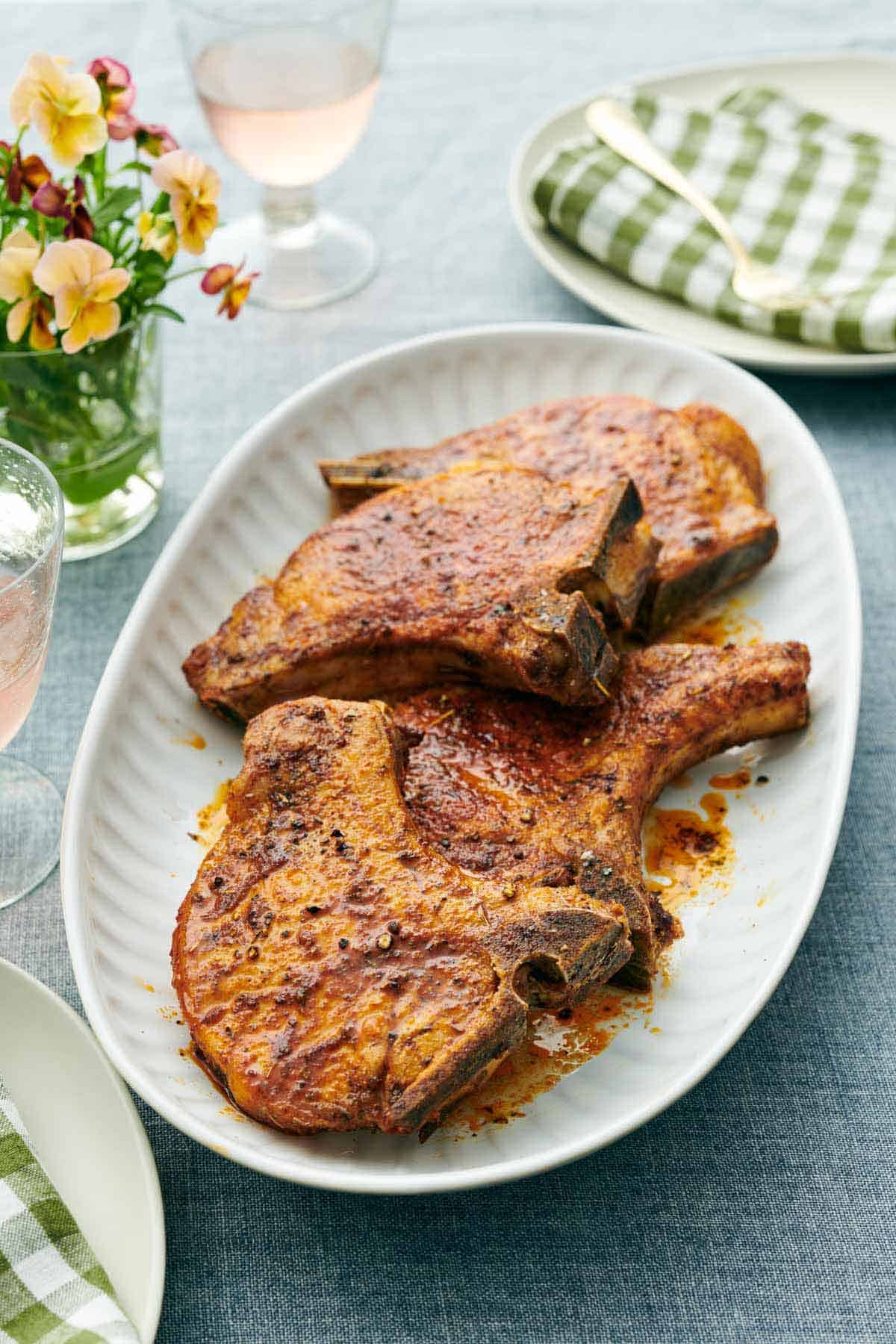 A platter with four air fryer pork chops. Drinks, flowers, and plates around the platter.