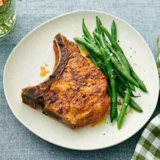 A plate with a juicy air fryer pork chop with green beans. A napkin and flowers off to the side.