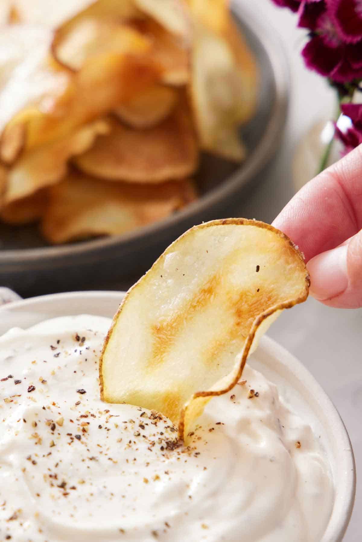 An air fryer potato chip dipped into a dip. More chips in the background.