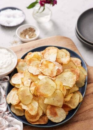A platter of air fryer potato chips. Some salt, pepper, dip, and plates on the side.
