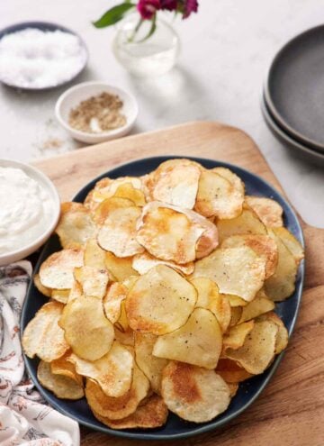 A platter of air fryer potato chips. Some salt, pepper, dip, and plates on the side.