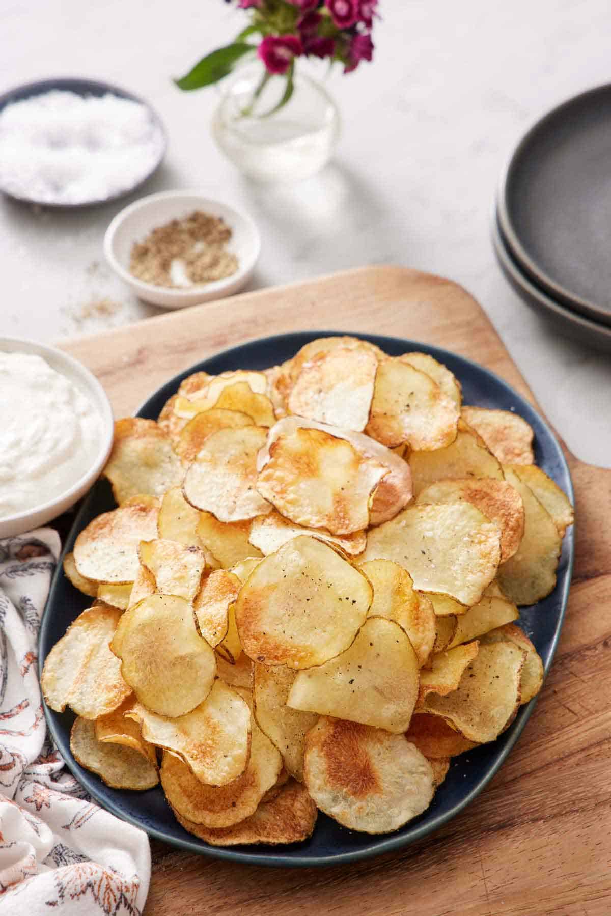 A platter of air fryer potato chips. Some salt, pepper, dip, and plates on the side.