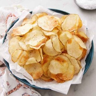 A pile of air fryer potato chips on a parchment lined plate. A linen napkin beside it.