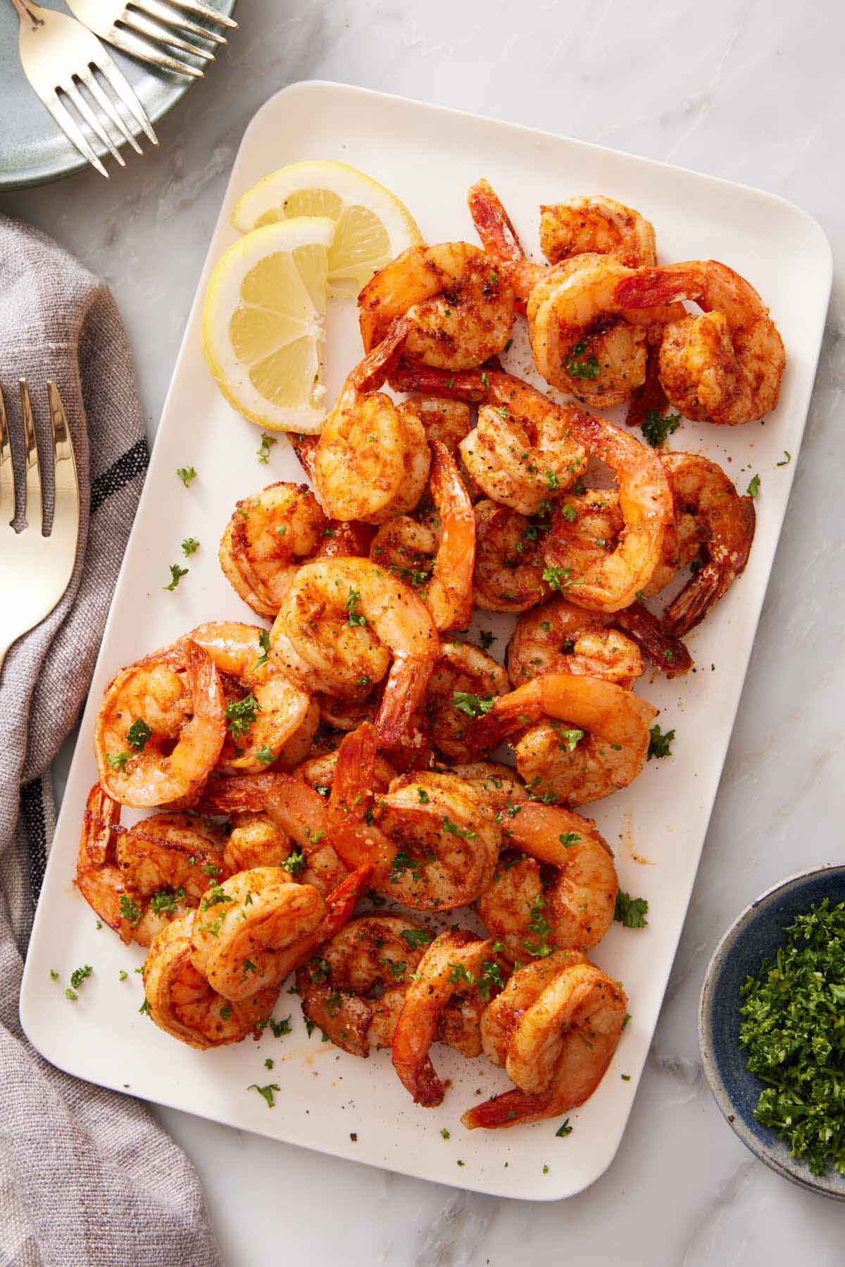 Overhead view of a platter of air fryer shrimp topped with parsley and lemon slices.