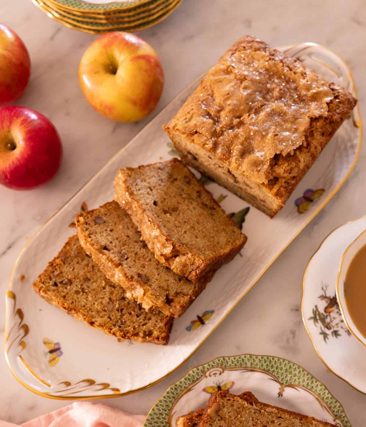 Overhead view of a loaf of apple bread with three slices cut out. Apples on the side and plates.