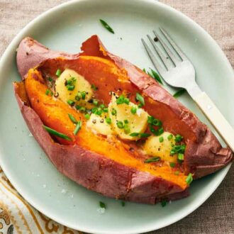 Overhead view of a green plate with a baked sweet potato topped with chives, pepper, and butter. A fork beside the potato.