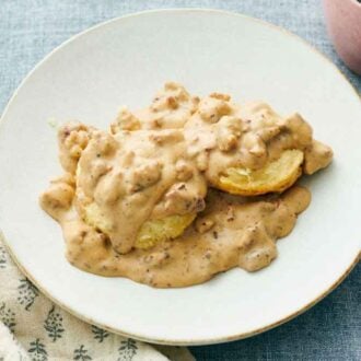 A white plate of biscuits and gravy with a pink mug and linen napkin beside it.