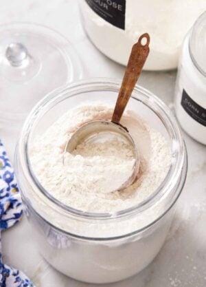 A large jar of cake flour substitute with a measuring cup inside. Two more jars of flours in the background.