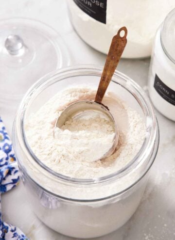 A large jar of cake flour substitute with a measuring cup inside. Two more jars of flours in the background.